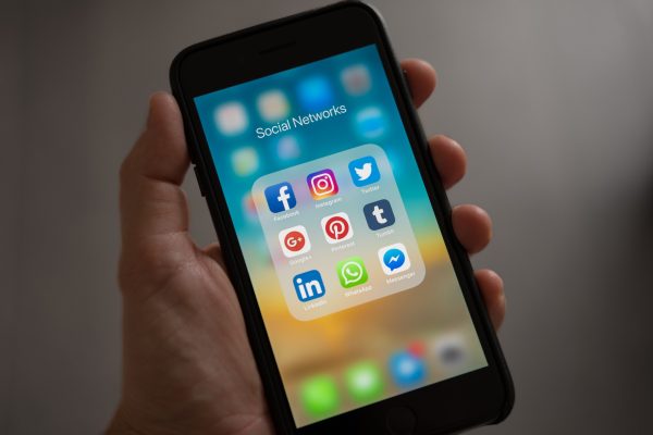mão segurando iphone desbloqueado com tela mostrando pastas com ícones de redes sociais