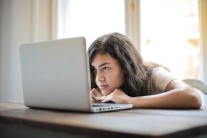 menina sentada encarando a tela do notebook e tendo um bloqueio criativo